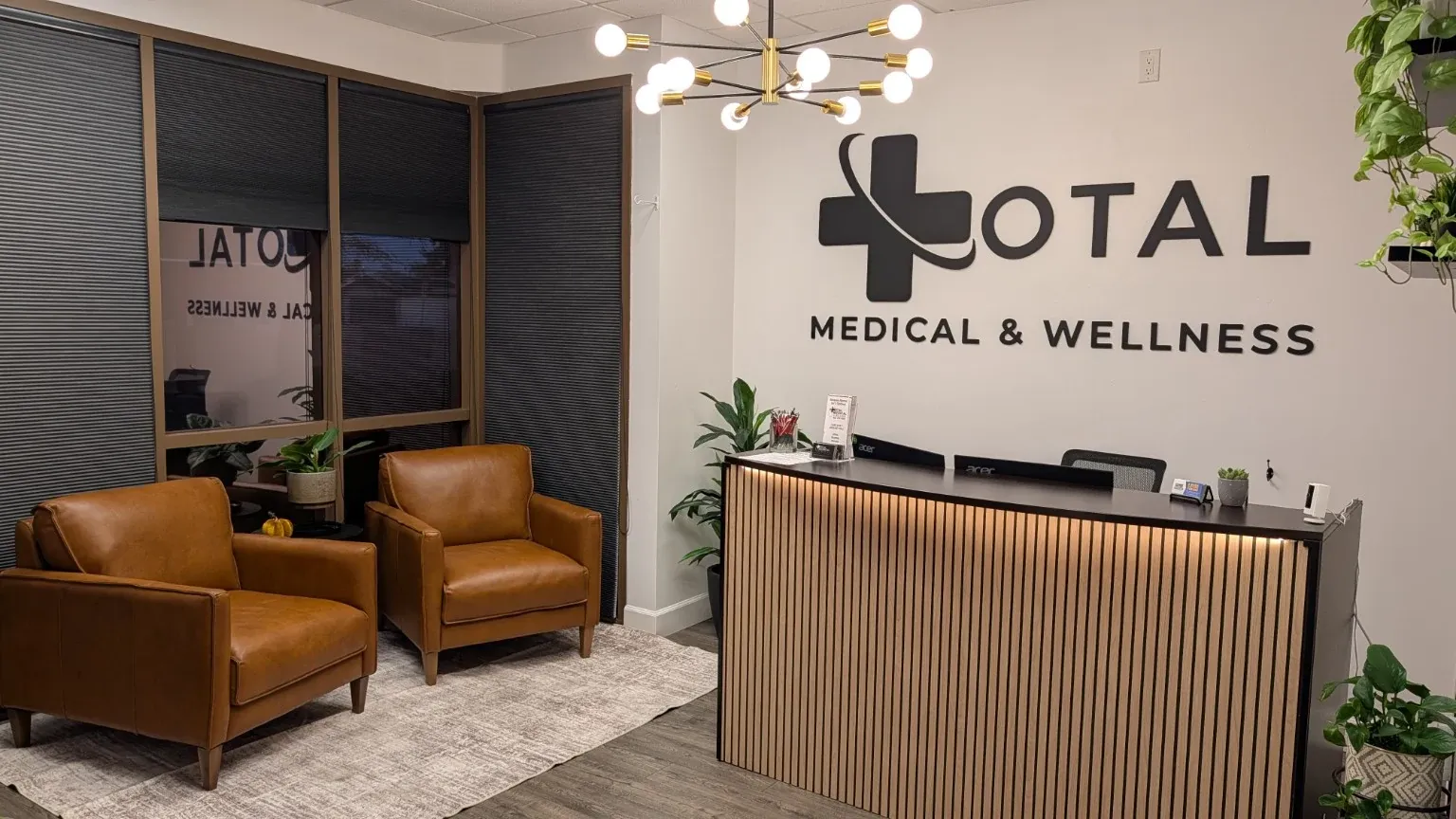 The reception and waiting area at Total Medical & Wellness in Glendale, Arizona, with cognac chairs and a wood-slat front desk.