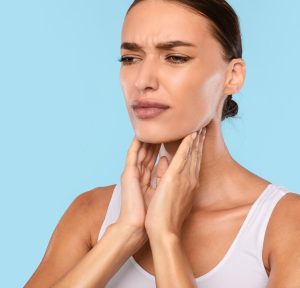 Young woman suffering from sore throat, blue studio